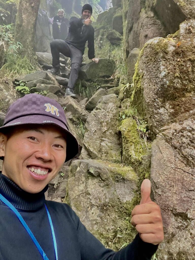 Trekker smiling and giving a thumbs up while climbing the rocky trail on Fansipan, Vietnam.